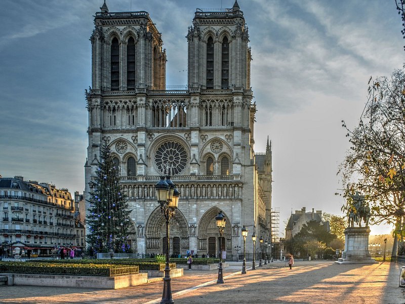 Notre-Dame de Paris and its rebuilt spire at dusk, with a Christmas tree on the square