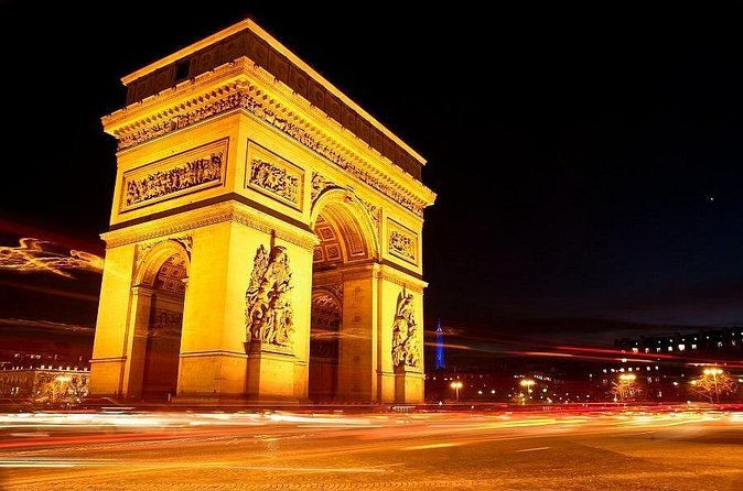 The Arc de Triomphe floodlit amber with traffic trails curving around it