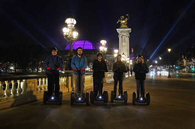 Riders pausing beneath the gilded lamps of Pont Alexandre III after dark