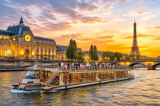 A Seine cruise boat on the water at sunset with the Eiffel Tower behind
