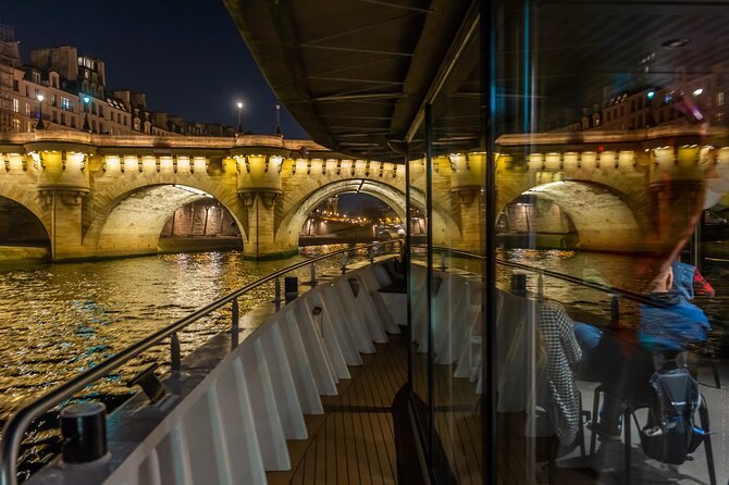 A lit cruise boat passing under the arches of the Pont Neuf at night